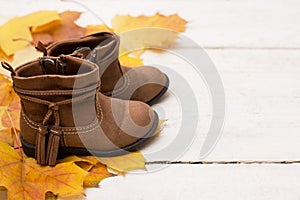 Female brown shoes satanding on white wooden table with yellow autumn leaves