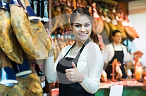 Female brunette selling jamon in delicatessen store