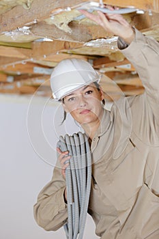 Female builder installing cable into roof space