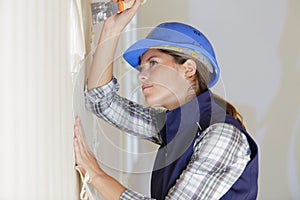 female builder removing wallpaper with scraper