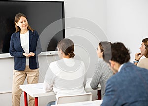 Female business coach gesturing with hand while standing against group of people sitting at chairs in front of her