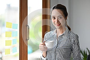 Female business leader holding coffee cup and smiling to camera.