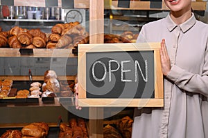 Female business owner holding OPEN sign in bakery