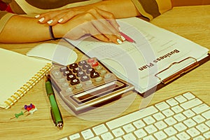 Female with Business plan, calculator and pen on the table. Woman working in office, sitting at desk, using computer