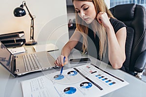 Female businesswoman readind financial report analyzing statistics pointing at pie chart working at her desk