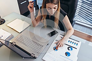 Female businesswoman readind financial report analyzing statistics pointing at pie chart working at her desk