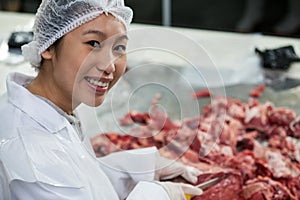 Female butcher cutting meat at meat factory