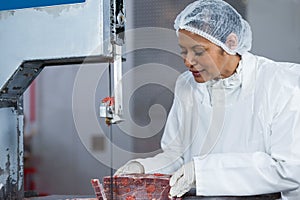 Female butcher cutting raw meat on a band saw machine