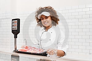 Female butcher weighing meat in supermarket.