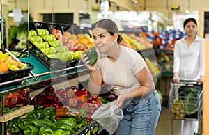 Female buyer selects ripe bell peppers in the vegetable section of supermarket
