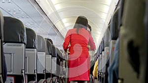 Female cabin crew with service cart serving passengers in aircraft corridor. flight attendant in red uniform working at airplane a