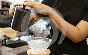 A female cafe operator wearing an apron pours hot water over roasted coffee grounds to prepare coffee for customers in the shop