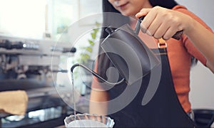 A female cafÃ© operator wearing an apron pours hot water over roasted coffee grounds to prepare coffee for customers in the shop