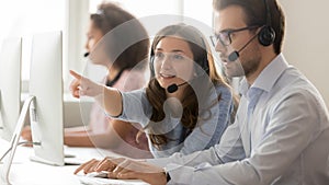 Female call center agent helping male colleague pointing at computer