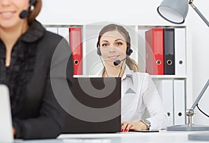 Portrait of smiling pretty female help desk employee with headset at workplace.