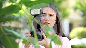 Female with camera hiding behind trees, journalist searching for sensation