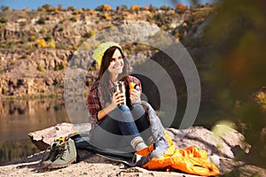 Female camper with thermos sitting on sleeping bag