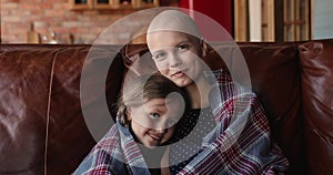 Female cancer patient her little daughter resting on sofa indoor