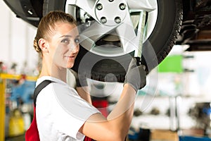 Female car mechanic working on jacked auto