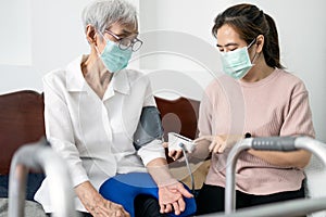 Female caregiver checking blood pressure measurement for the  senior woman at home during the Covid-19 outbreak,asian elderly photo