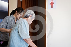 Female caregiver is helping support elderly woman walk into the restroom carefully,asian senior with bladder control problem need