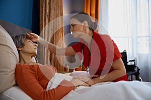 Female caregiver measuring temperature touching forehead of old woman