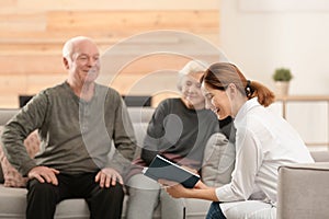 Female caregiver reading book to elderly spouses