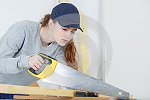 Female carpenter cutting plank with handsaw