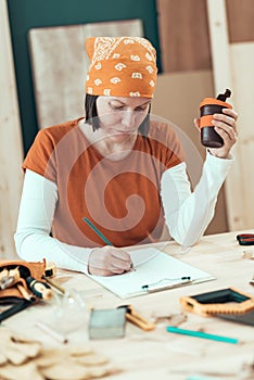 Female carpenter is drinking coffee and planning DIY project