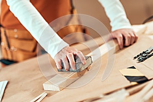 Female carpenter manually sanding wooden plank photo