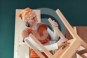 Female carpenter repairing wooden chair seat in workshop