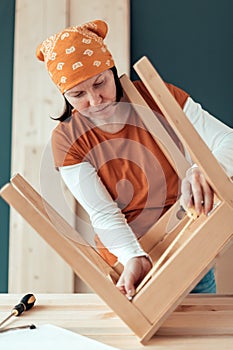 Female carpenter repairing wooden chair seat in workshop