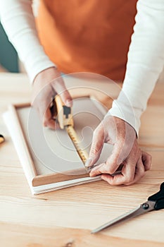 Female carpenter tape measuring picture frame in workshop