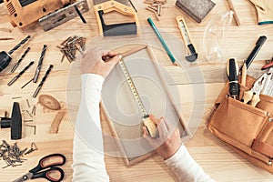 Female carpenter tape measuring picture frame in workshop photo