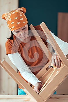 Female carpenter tape measuring wooden chair seat in workshop