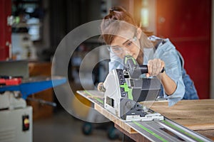A female carpenter uses a chainsaw while working in a wood shop