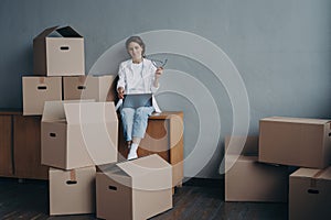 Female with carton boxes searching moving company at laptop for relocation. Transportation service