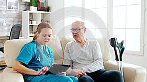 Female caucasian nurse taking notes about elderly man health in bright and cozy nursing home