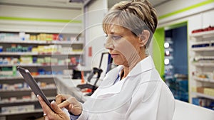 Female caucasian pharmacist scrolling on digital tablet searching for prescriptions for customers in pharmacy