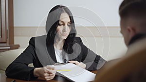 Female Caucasian psychologist showing sad face on paper and talking to blurred man in office. Portrait of confident