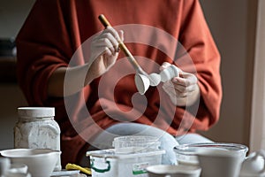 Female ceramicist or potter holding paintbrush applying glaze on ceramic pieces photo