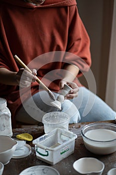 Female ceramicist or potter holding paintbrush applying glaze on ceramic pieces photo