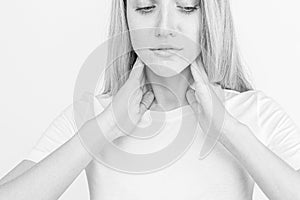 Female checking thyroid gland by herself. Close up of woman in white t- shirt touching neck with red spot. Thyroid