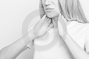 Female checking thyroid gland by herself. Close up of woman in white t- shirt touching neck with red spot. Thyroid