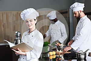 Female chef checking recipe in book by her