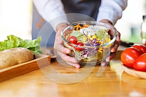 A female chef cooking and holding a bowl of fresh mixed vegetables salad in kitchen