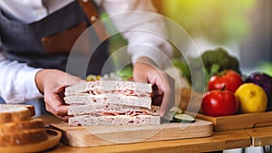 A female chef cooking and holding a piece of whole wheat ham cheese sandwich in kitchen