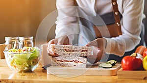 A female chef cooking and holding a piece of whole wheat ham cheese sandwich in kitchen