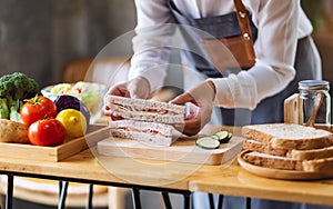 A female chef cooking and holding a piece of whole wheat ham cheese sandwich in kitchen