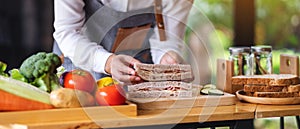 A female chef cooking and holding a piece of whole wheat ham cheese sandwich in kitchen